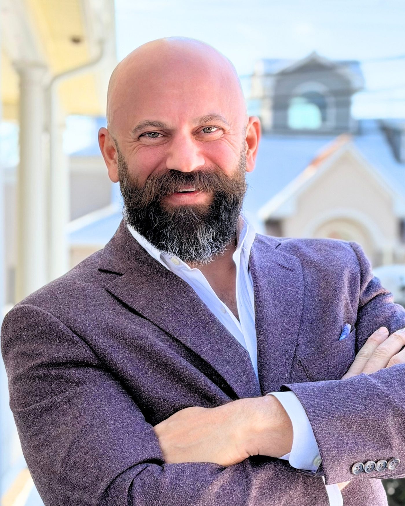 Filipos Halikias, arms crossed, in a plum tweed blazer on a Victorian porch in Bucks County.